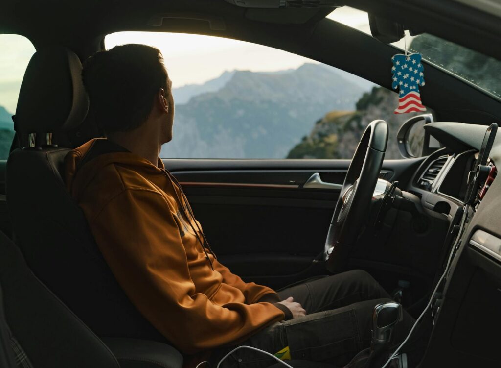 The Best Car Air Freshener for a Fresh-Smelling Ride 3 A man in a car admires the scenic mountain view through the window, wearing a casual hoodie.