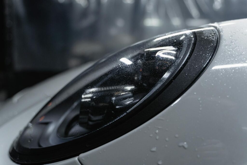 Is a Monthly Car Wash Membership Worth It? 2 Detailed shot of a sleek car headlight with water droplets enhancing its glossy surface.