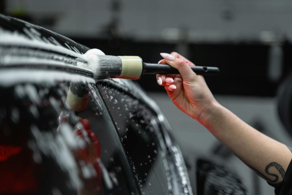 Should You Wash Your Car After Car Waxing or Coating? 1 Hand cleaning car exterior with brush and foam in a detailed car wash process.
