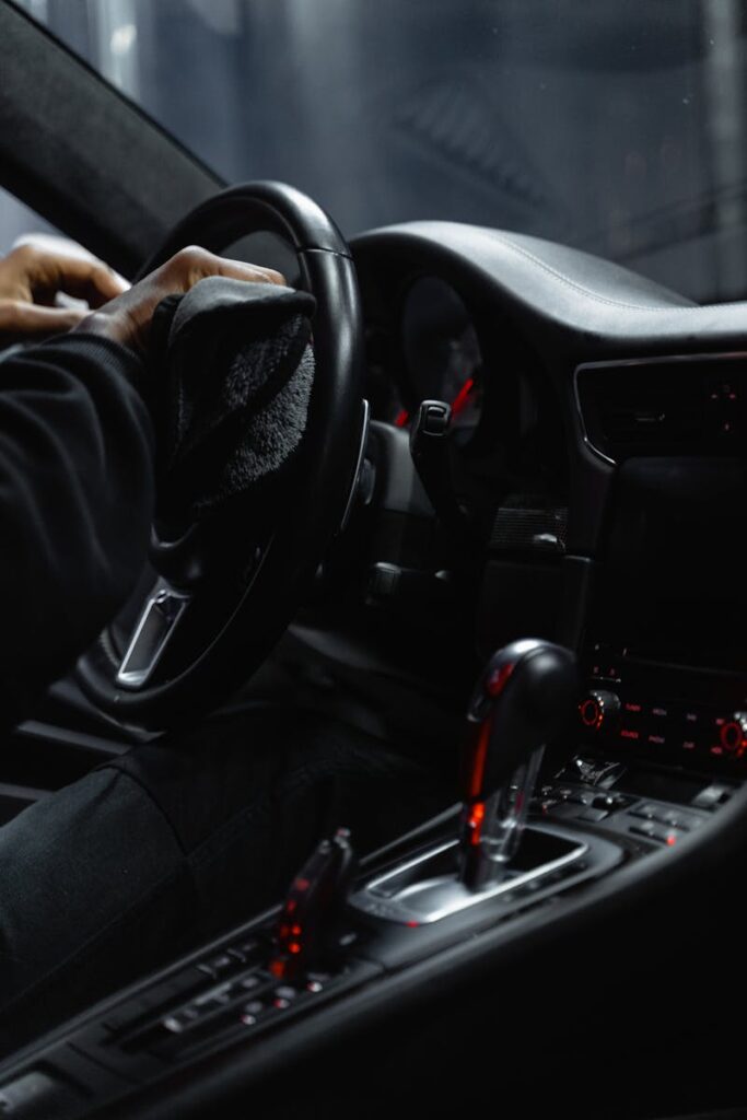 The Best Car Interior Cleaning Products We Recommend for Frederick Families 1 Close-up of a person cleaning a car's dashboard and steering wheel, focused on interior maintenance.