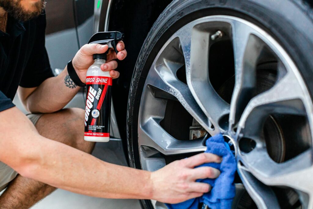 Top Car Cleaning Supplies for At-Home Care in Frederick, MD When You Can't Head To Fusion Car Wash 1 A person cleans a car wheel using a spray bottle and a cloth, ensuring a polished finish.