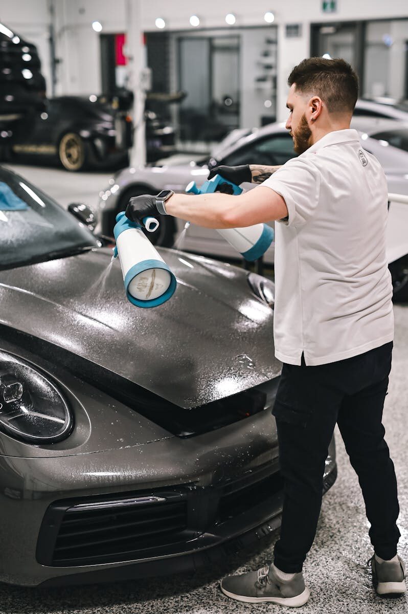 Man polishing luxury sports car with spray in a professional workshop.