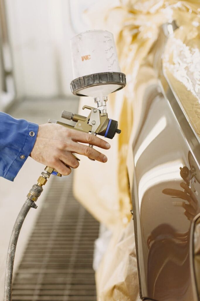 A technician spray paints a car with a paint spray gun in a workshop.