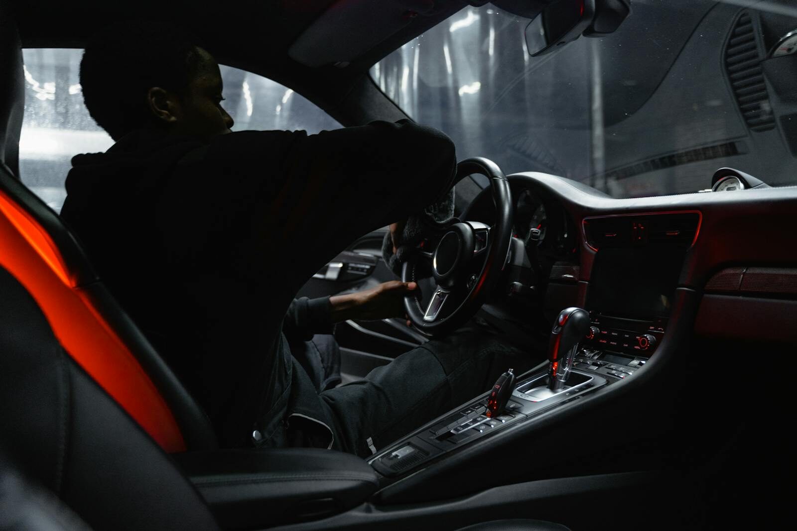 African American man cleaning luxury car interior with focus on steering wheel and dashboard.
