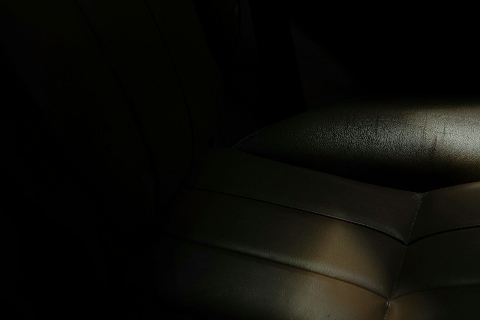 Photo by Ansis Kančs A dark, leather sofa corner is barely illuminated.