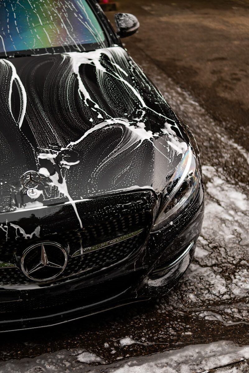 Black car covered in soap suds during wash.