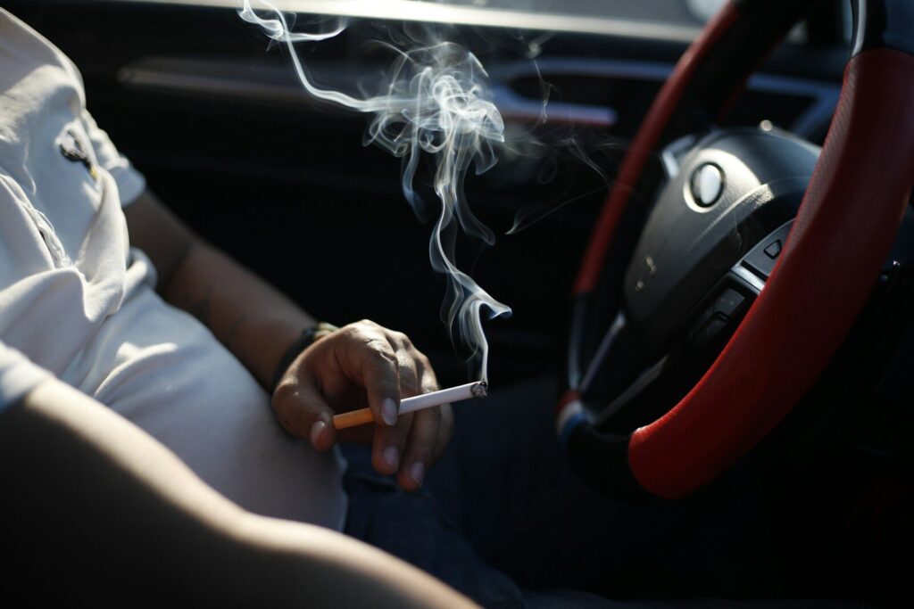 How To Get Smoke Smell Out Of Car Interior And Breathe Easy 1 person holding cigarette stick in front of car steering wheel