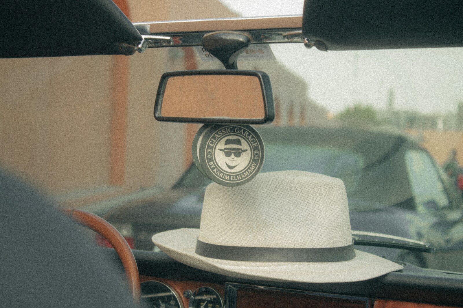 White fedora hat rests on car dashboard with rearview mirror.