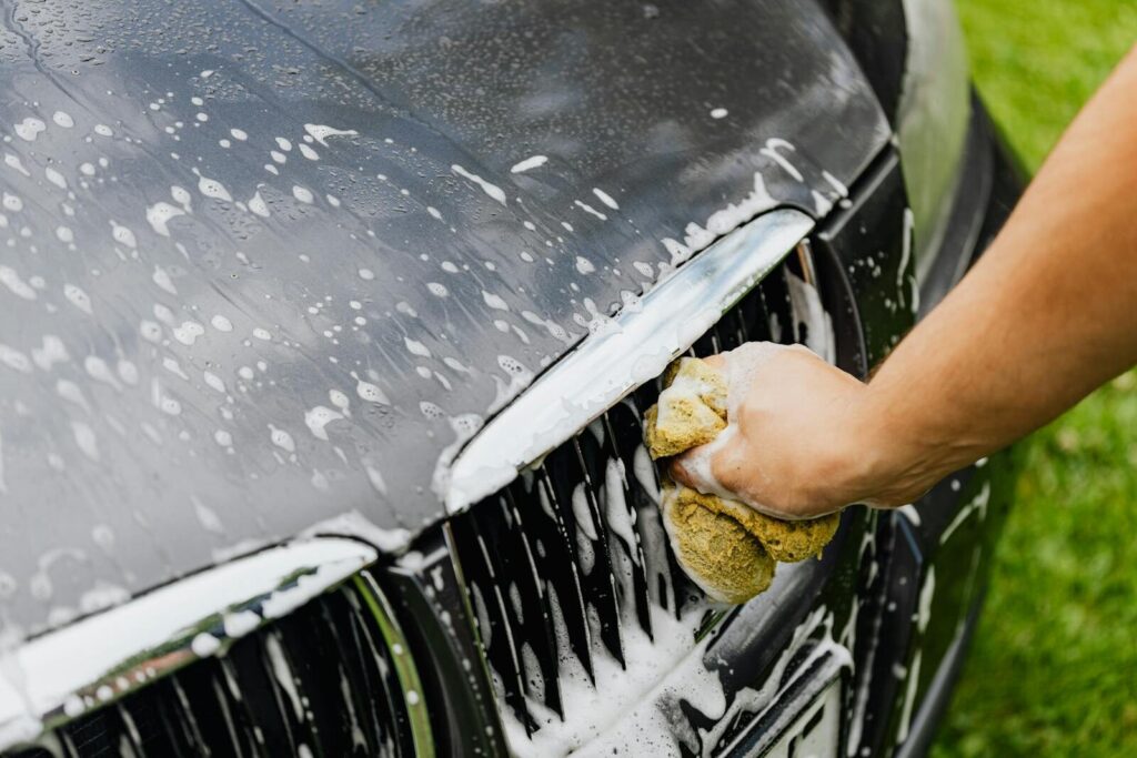 Can You Use Dish Soap to Wash Your Car? What Frederick Drivers Should Know 2 Detailed view of a hand washing a car grille with a soapy sponge outdoors.