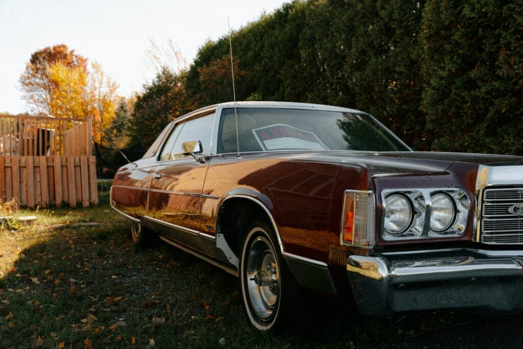 Vintage maroon car parked outdoors near trees.